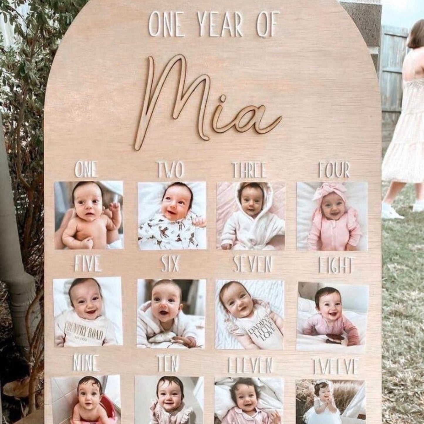 Wooden photo display with 'One Year of Mia' text and baby photos arranged in a grid.