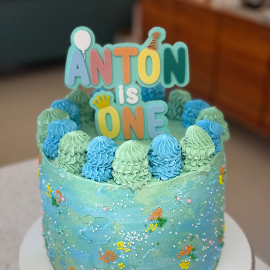 Birthday cake with 'ANTON is ONE' topper on a countertop.