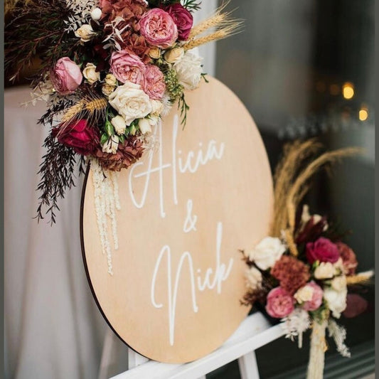 Decorative sign with floral arrangements and 'Alicia & Nick' text on a blurred background