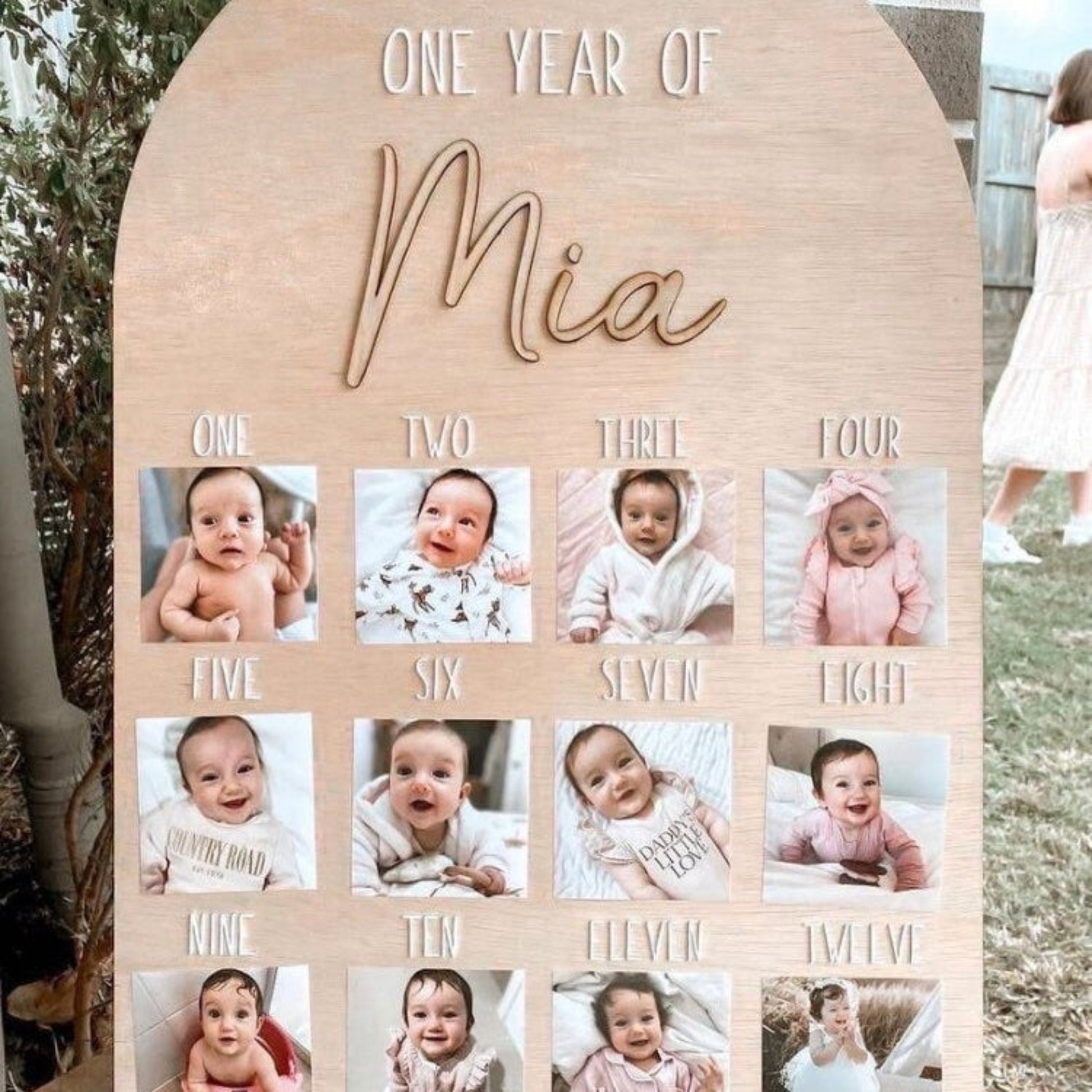 Wooden photo display with 'One Year of Mia' text and baby photos arranged in a grid.