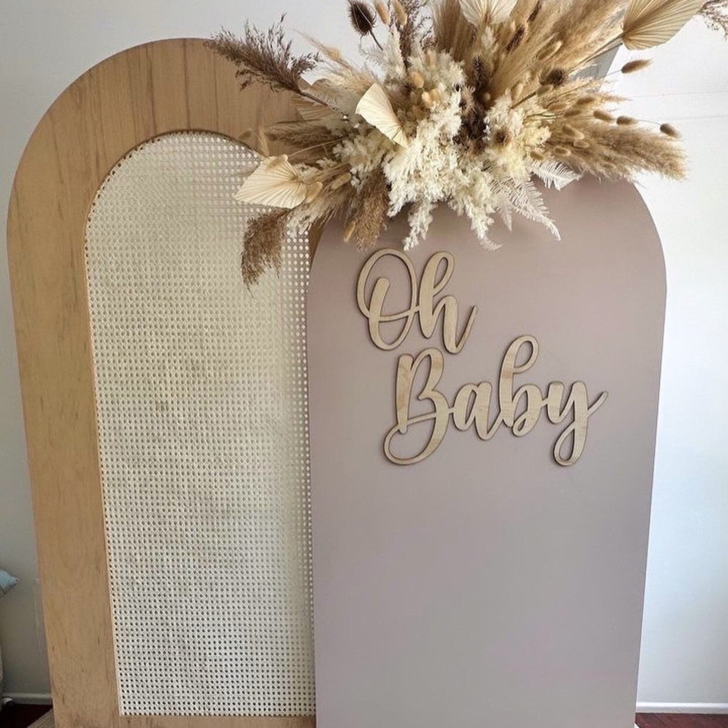 Decorative arch with 'Oh Baby' sign and dried flowers on a neutral background