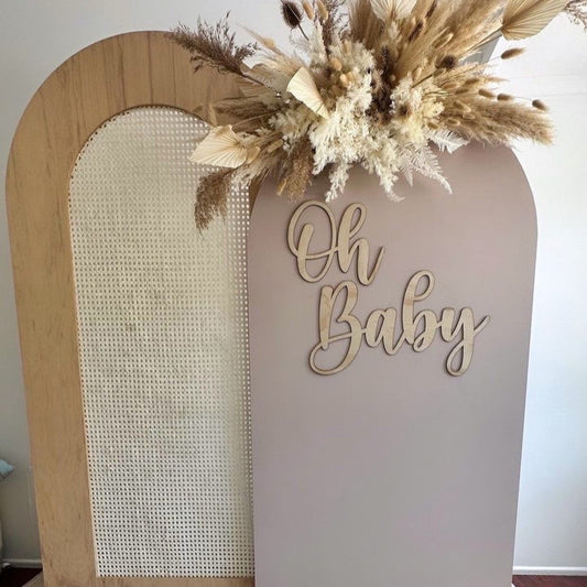 Decorative arch with 'Oh Baby' sign and dried flowers on a neutral background