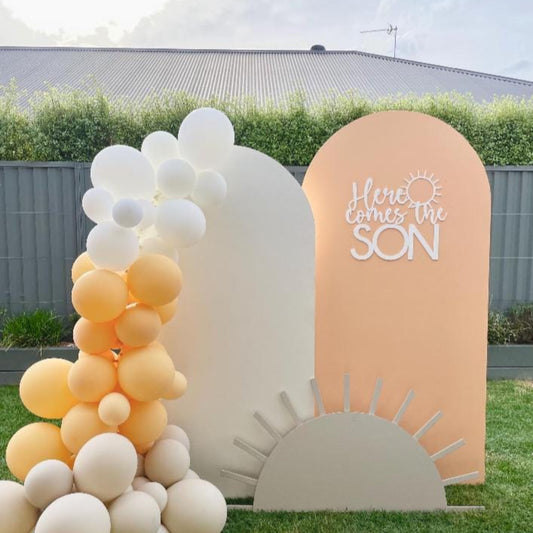 Decorative arch with balloons and 'Here Comes the Son' sign outdoors.